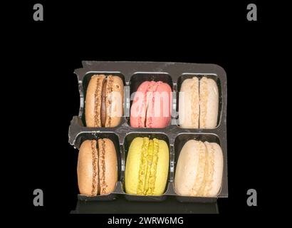 Diversi macaron dolci su un vassoio di plastica, macro, isolati su sfondo nero. Foto Stock