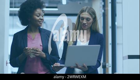 Due colleghe stanno discutendo di qualcosa mentre si cammina e si utilizzano i laptop in un ufficio Foto Stock