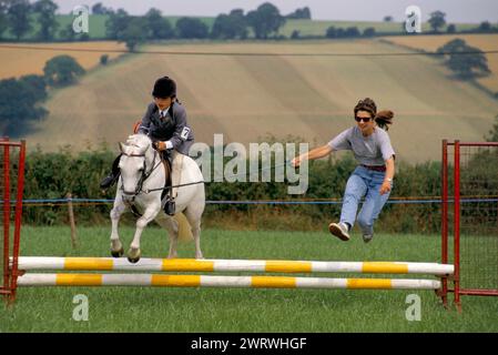 Pony club gymkhana madre e figlia in competizione insieme. Figlia che sta guidando il suo pony. Madre che corre per il corso assicurandosi che il bambino faccia bene. Anni '1990 Regno Unito. Quantock Hills, Somerset. 1997 HOMER SYKES Foto Stock