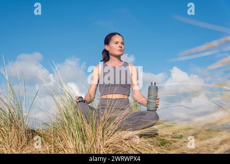 vestibilità donna sportiva seduta a gambe incrociate al sole con una bottiglia d'acqua. Foto Stock