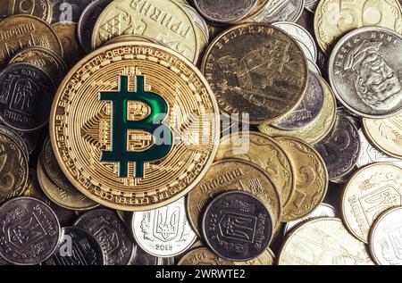 Foto della moneta bitcoin d'oro che giace su una pila di monete ucraine. Foto Stock