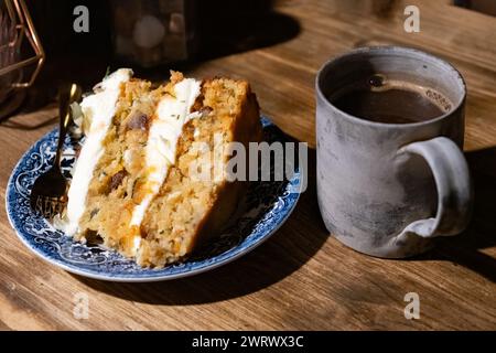 Una fetta appena sfornata di una torta vegana a strati di carote e zucchine. La torta è servita su un tavolo da caffè con una tazza di caffè nero fresco Foto Stock