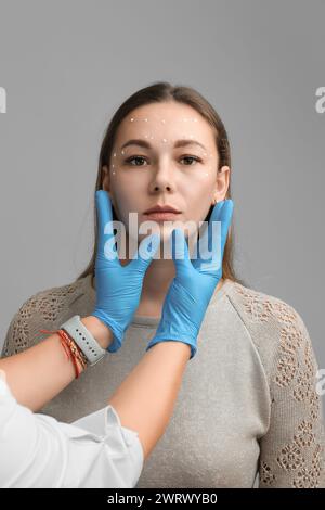 Il volto di una giovane ragazza con crema o maschera applicata sulla pelle e le mani di un cosmetologo in guanti. Concetto di cura della pelle, ringiovanimento, pulizia Foto Stock