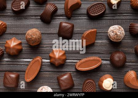 Diverse caramelle al cioccolato su una texture di legno scuro sfondo vista dall'alto. Dolci assortiti sul tavolo. Cioccolatini scuri e al latte. Dessert al cioccolato. Foto Stock