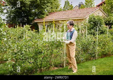 donna matura e sofisticata, gioiosa, con capelli corti e un abbigliamento elegante e vivace, che si prende cura delle sue piante Foto Stock