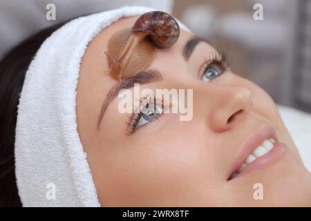 Procedura cosmetologica. Bella giovane donna con una lumaca ahatin sul viso in un salone di bellezza. Foto Stock