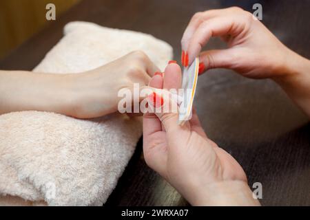 Il maestro della manicure seziona e attacca una forma di chiodo durante la procedura di estensione delle unghie con gel nel salone di bellezza. Assistenza professionale Foto Stock