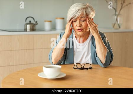 Mal di testa. Donna anziana infelice di mezza età che soffre di mal di testa malata che sfrega le tempie a casa. Anziana nonna anziana matura che tocca i templi che sperimenta stress donna che sente dolore alla testa Foto Stock