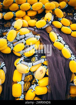 I vivaci carri gialli intrappolati nelle tradizionali reti da pesca, catturati nel vivace porto, simboleggiano l'industria marina. Foto Stock