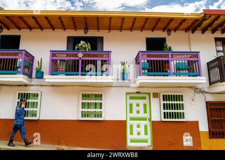 Jerico, Colombia - 14 gennaio 2023: L'agente di polizia colombiano cammina parlando al telefono di fronte a una casa colorata Foto Stock