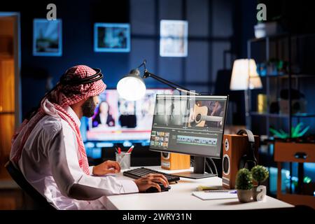 Un uomo del Medio Oriente modifica informazioni video sullo schermo del suo computer utilizzando software multimediali. Il regista di Arab Guy lavora a un montaggio su un monitor di un computer in questa immagine a vista laterale. Foto Stock