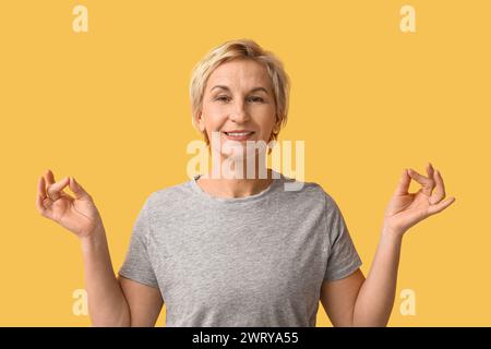 Ritratto di una donna matura meditata su sfondo giallo Foto Stock