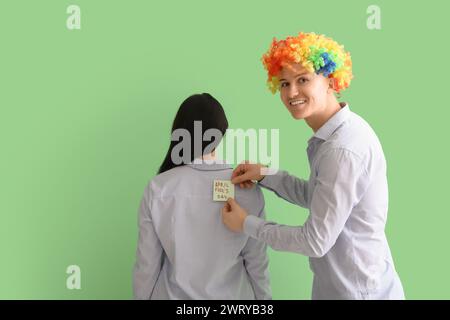 Uomo d'affari che attacca carta sulla schiena del suo collega su sfondo verde. Festa del Fool's Day di aprile Foto Stock