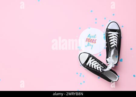 Scarpe con lacci legati, cartolina natalizia e coriandoli su sfondo rosa. Festa del Fools Day di aprile Foto Stock