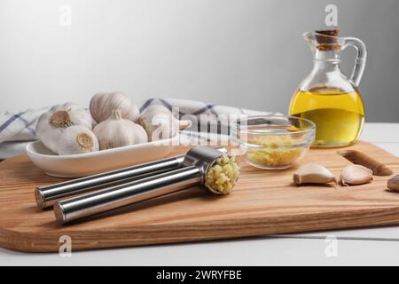 Una pressa in metallo e aglio schiacciato su un tavolo di legno bianco Foto Stock