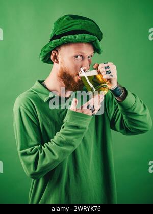 Fascino fortunato su sfondo verde. Cappello di leprechauns. L'uomo su sfondo verde festeggia il giorno di San Patrizio. Ritratto di uomo eccitato che tiene un bicchiere di birra sopra Foto Stock