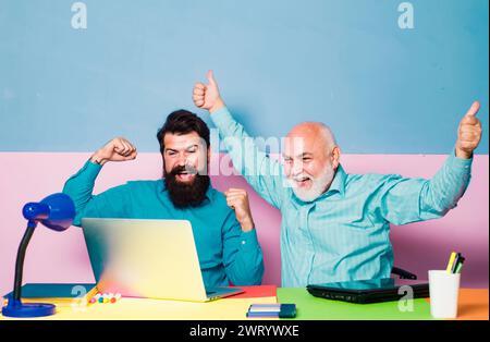 Ritratto in vita di due bellissimi uomini d'affari seduti al tavolo con un computer portatile nell'interno dell'ufficio. Lavoro di squadra e concetto di partnership per uomini d'affari. Foto Stock