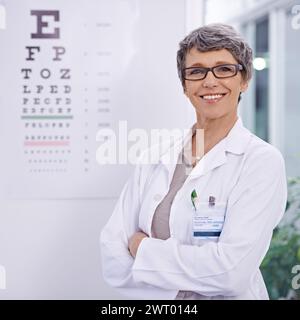 Donna, optometrista senior e braccia incrociate per la cura degli occhi in verticale, test e grafico alfabetico per la visione. Occhiali, lenti e montatura per Foto Stock