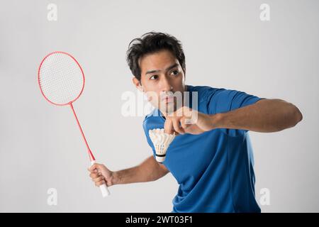 Un giocatore di badminton in abbigliamento sportivo regge una racchetta e un rubinetto sullo sfondo bianco. Foto Stock