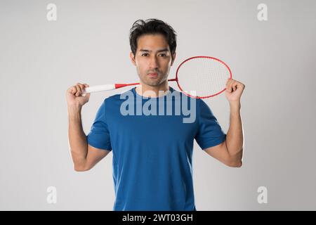 Giocatore di badminton che indossa un abbigliamento sportivo in piedi con una racchetta sullo sfondo bianco. Foto Stock