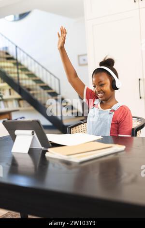 Una giovane ragazza afroamericana alza la mano durante una lezione virtuale a casa Foto Stock