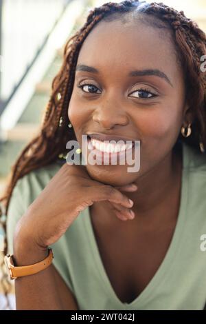 Una giovane donna afroamericana sorride brillantemente, appoggiando il mento sulla mano a casa Foto Stock