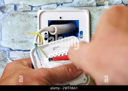 Cablaggio della nuova presa elettrica del termostato nella parete in pietra, installazione da parte di elettricista, collegamento dei fili di massa e neutro sotto tensione, interventi relativi all'elettricità Foto Stock