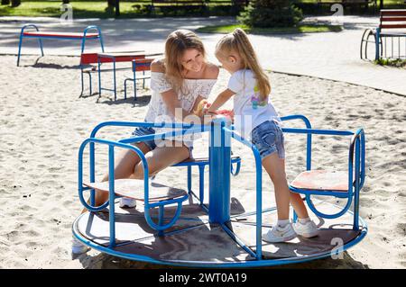 Madre e figlia giocano nel parco giochi nel parco cittadino estivo. Concetto di infanzia, tempo libero e persone - buon riposo in famiglia e buon divertimento Foto Stock