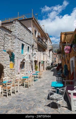 Una vista soleggiata del vicolo con caffetterie e tradizionali edifici in pietra sotto un cielo blu parzialmente nuvoloso, vicoli nella città vecchia, Areopoli, Areopolis Foto Stock