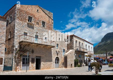 Edifici in pietra su una strada trafficata del villaggio con passanti sotto un cielo blu con nuvole, città vecchia, Areopoli, Areopolis, Tsimova, Itylo, Anatoliki mani Foto Stock