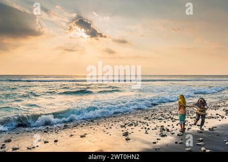 Donna musulmana al sole della sera sulla spiaggia di Mangsit a Sengiggi, Islam, religione, velo, viaggi, turismo, mare, spiaggia, acqua, rispetto, drammatico Foto Stock