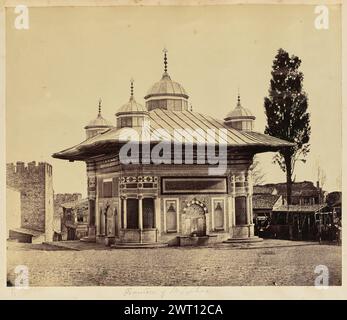 Fontana del Sultano Ahmed III Sconosciuto, fotografo anni '1850-'1890 veduta della fontana del sultano Ahmed III fuori dalla porta Imperiale del Palazzo Topkapi. Il tetto dell'edificio presenta quattro cupole visibili e si estende oltre le pareti. Le pareti dell'edificio sono coperte da intricati intagli, piastrelle e scritte arabe dipinte. Quattro delle fontane sono visibili, due su ciascun lato dell'edificio. Le torri e le mura che circondano il palazzo possono essere viste dietro la fontana lungo il lato sinistro dell'immagine, e gli edifici più piccoli e le case della città possono essere visti lungo la sid destra Foto Stock