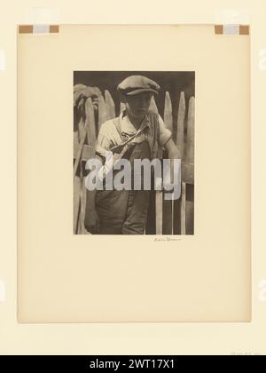 Ragazzo in piedi di UnPainted Fence. Doris Ulmann, fotografo (americano, 1882 - 1934) 1925–1934 ritratto di un giovane ragazzo di tre quarti di lunghezza. Viene ruotato di tre quarti verso destra. Indossa un berretto, una camicia bianca con maniche arrotolate e tute. È appoggiato su una recinzione di legno, il suo gomito sinistro poggiato sulla ringhiera. Foto Stock