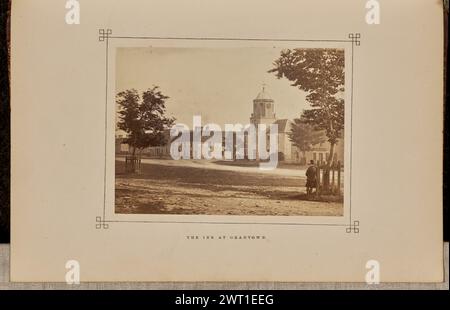 La locanda di Grantown. George Washington Wilson, fotografo (scozzese, 1823 - 1893) 1868 Vista degli edifici di Grantown-on-Spey lungo un'ampia strada sterrata, incluso il Grant Arms Hotel, che presenta il suo nome dipinto su un bordo bianco vicino al tetto. Un uomo sta accanto a un albero circondato da una recinzione sul lato destro dell'immagine. (Recto, monta) parte centrale inferiore, stampa con inchiostro nero: "THE INN AT GRANTOWN". Foto Stock