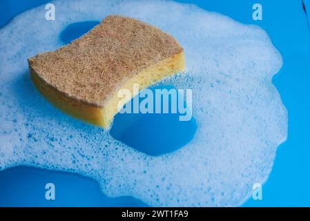 Spugna gialla con sapone e schiuma su sfondo blu. Concetto di pulizia. Copia spazio Foto Stock