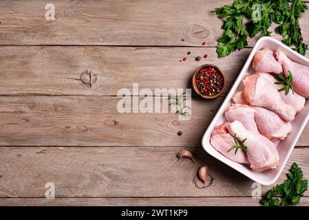 Cosce di pollo crude in teglia da forno con erbe, spezie e aglio pronte per la cottura in forno, sfondo in legno, vista dall'alto, spazio copia. Preparazione dell'orga cruda Foto Stock