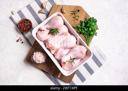 Cosce di pollo crude in teglia da forno con erbe, spezie e aglio pronte per la cottura in forno, sfondo bianco, vista dall'alto, spazio copia. Preparazione dell'organo grezzo Foto Stock
