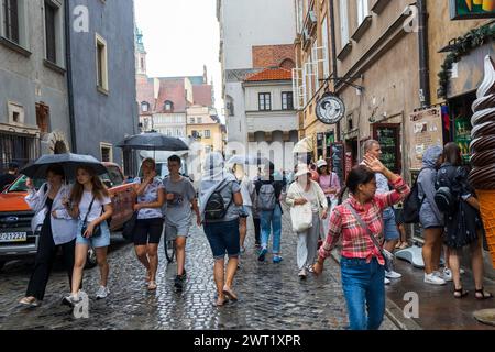 Varsavia, Polonia - 23 agosto 2023, le persone camminano con ombrelloni sotto la pioggia attraverso la città vecchia. Foto Stock