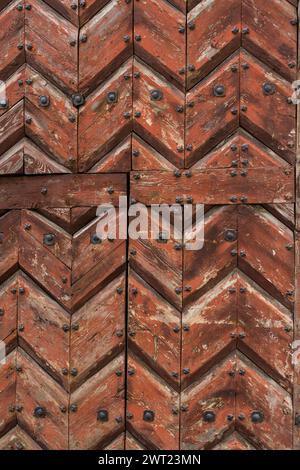 porta in legno verniciata marrone composta da tavole zigzag. si tratta di una fodera chiodata con rivetti o chiodi metallici Foto Stock