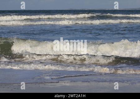 Onde con creste bianche inondare la spiaggia sabbiosa Foto Stock