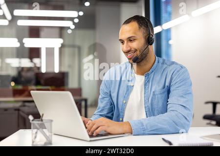 Un agente del servizio clienti di sesso maschile felice con una cuffia che lavora al computer in un ufficio moderno e che si occupa dell'assistenza clienti. Foto Stock