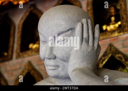 Primo piano della mano e della testa di una delle tante statue buddiste in pietra nel complesso di pagoda del tempio Bai Dinh a Ninh Binh, nel nord del Vietnam. Foto Stock