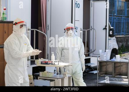 Due medici vestiti in tuta e maschere per proteggersi, aspettando nel cortile di un ospedale le persone che devono effettuare il test per il Foto Stock
