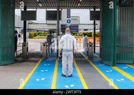 Gli operai, all'arrivo presso lo stabilimento Gian Battista Vico dell'industria automobilistica FCA (ex FIAT), appena riaperto, camminano lungo una pista con impronta Foto Stock