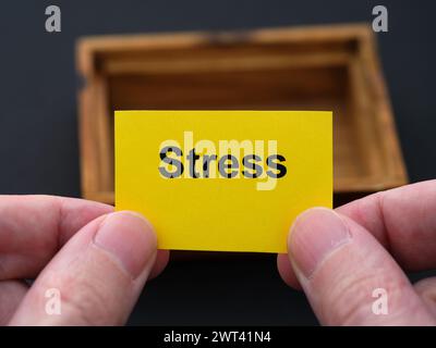 Un uomo che tiene in mano un pezzo di carta gialla con la parola "stress", sopra una piccola scatola di legno vuota. Primo piano. Foto Stock