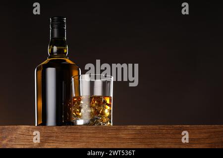 Whisky con cubetti di ghiaccio in vetro e bottiglia su un tavolo in legno, vista ad angolo basso. Spazio per il testo Foto Stock