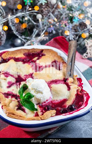 Ciabattino di frutti di bosco in teglia smaltata, guarnito con gelato, decorazione natalizia con bokeh su sfondo, verticale Foto Stock