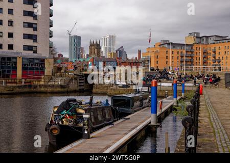 Le chiatte dei canali ormeggiate nel molo di Leeds, con persone sedute su gradini e edifici del centro città dietro, Leeds, West Yorkshire, Inghilterra. Foto Stock