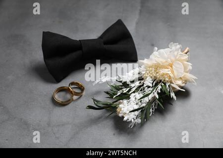 Roba per matrimoni. Elegante boutonniere, papillon e fedi nuziali su sfondo grigio Foto Stock