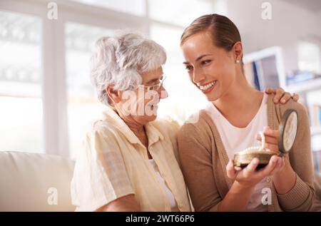 Confezione regalo, collana e madre anziana con donna sul divano per regalare e sorprendere in salotto. Famiglia, perle e figlia felice con mamma Foto Stock